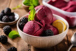 Brombeer-Limonaden-Sorbet in einer Glasschale, garniert mit frischen Brombeeren und Minzblättern, auf einem hellen Holztisch