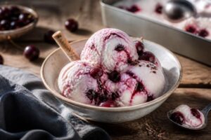 Kirsch-Quark-Eis ohne Eismaschine in einer cremefarbenen Gefrierbox, mit glänzenden Kirschen und Minzblättern garniert, von oben fotografiert
