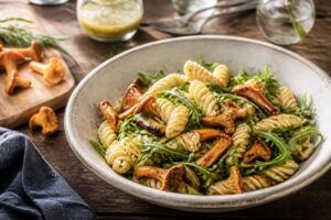 Pfifferling-Nudelsalat mit Rucola und Senf-Dressing in einer großen Schüssel, garniert mit frischen Kräutern